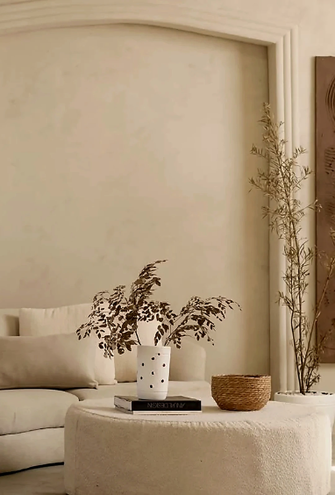 Outro enquadramento da sala clara com sofá curvo, mesa de centro e vegetação ornamental