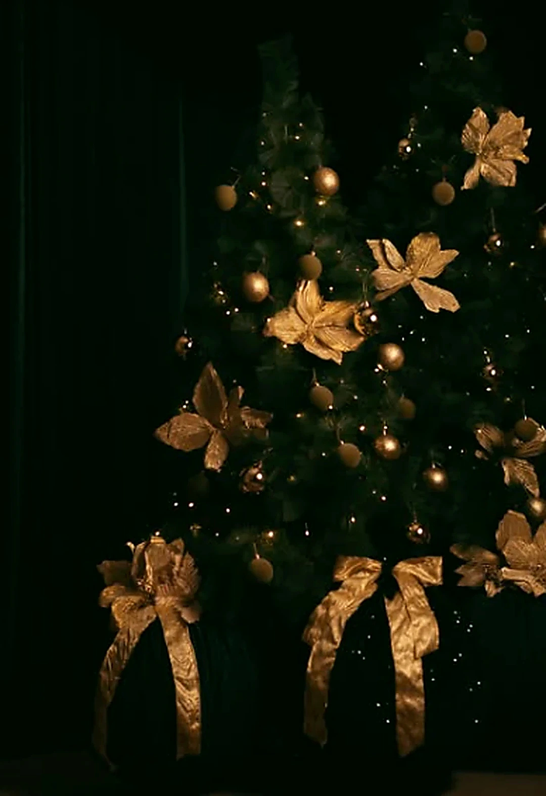 Árvore de Natal em ambiente escuro com ornamentos dourados e luzes pontuais