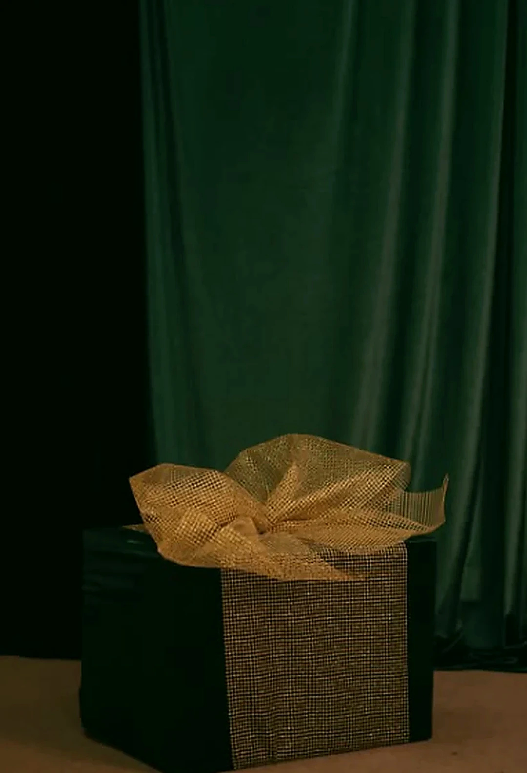 Presente de Natal preto com laço dourado diante de tecido verde-escuro